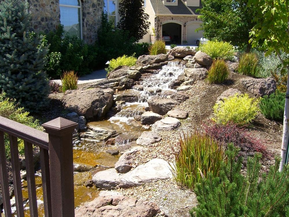 Serene garden stream with rocks and lush greenery, enhancing outdoor landscape design.