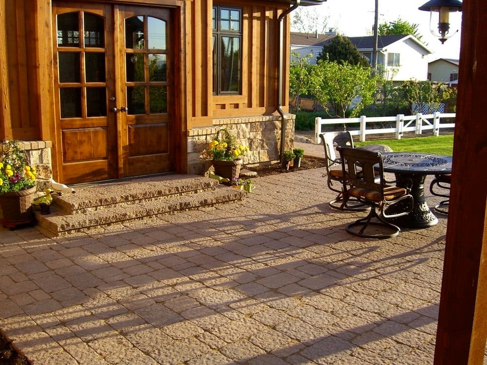 Patio area with stone steps, wooden doors, and potted plants near a house.